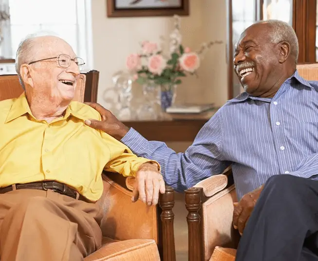 Two older men sitting on a chair and laughing.