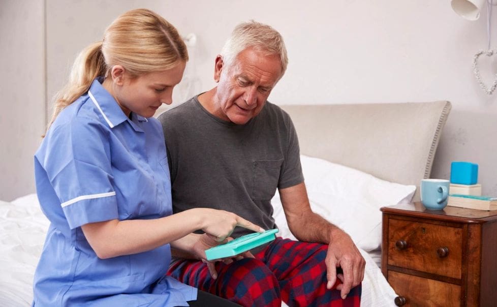 A nurse is helping an older man with his tablet.